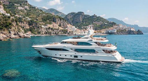 A side view of a majestic 42m luxury motor yacht cruising through the crystal clear turquoise waters of the Amalfi Coast. The sun reflects brilliantly off the polished white hull and large panoramic glass windows. The lighting is bright and warm, capturing the essence of a high-end Mediterranean summer afternoon with soft, airy blue highlights and pristine white tones.