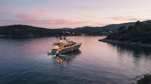 A serene dusk view of a luxury yacht anchored in a calm, secluded bay. The sky is painted in soft pastel pinks and purples, reflecting on the water. The yacht's deck lights are warmly illuminated. The image feels calm, luxurious, and nostalgic.