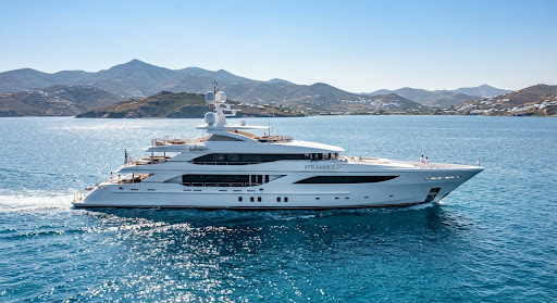A majestic side profile of the Stellaris II luxury yacht at sea. The hull is a pristine, glossy white that gleams under the bright midday sun. The background features the sparkling blue Aegean Sea and distant coastal mountains. The shot is high-contrast, clean, and exudes an air of premium exclusivity.